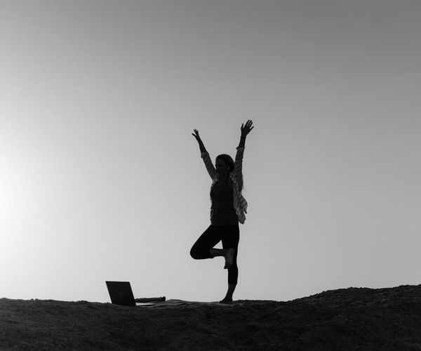 Silhouette of a person in a powerful yoga warrior pose at sunrise.